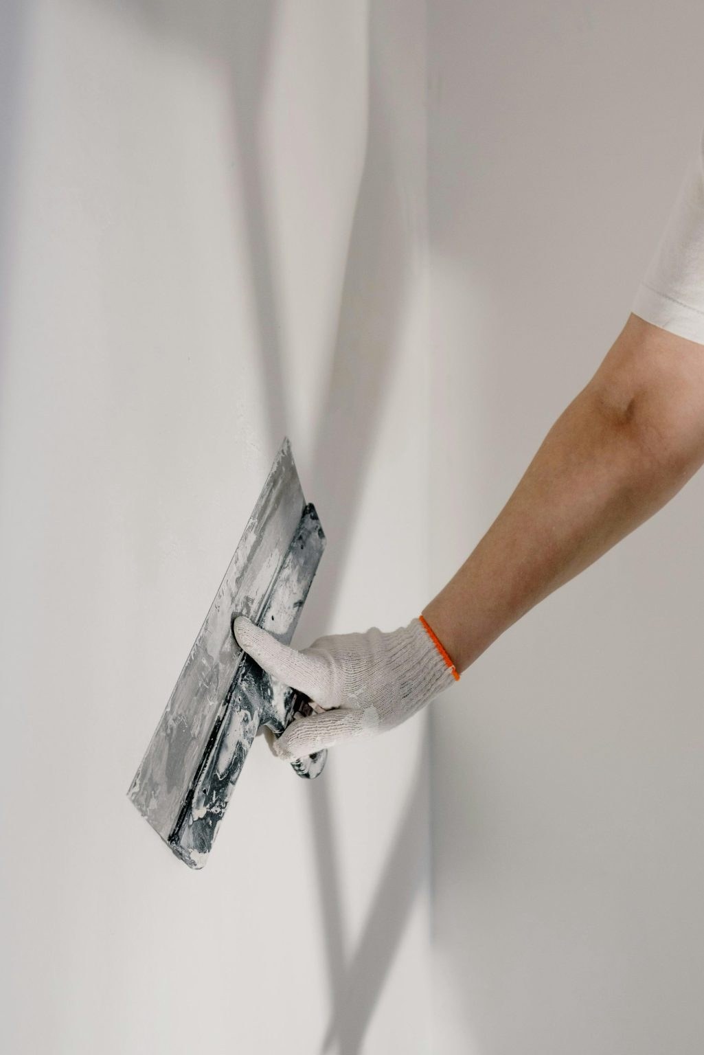A gloved hand smoothing a wall with a drywall trowel