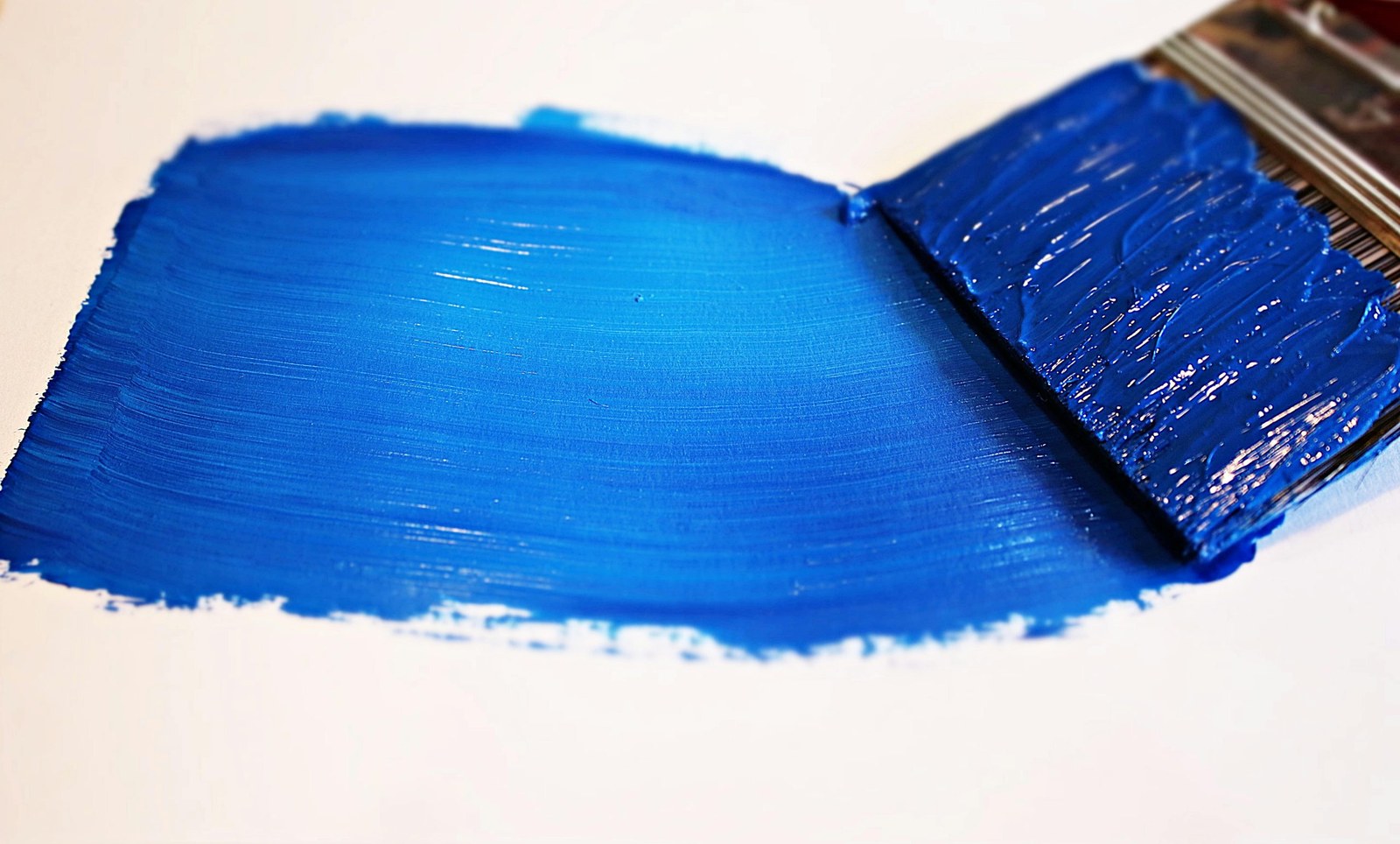 A brush laying down a bold stroke of blue paint